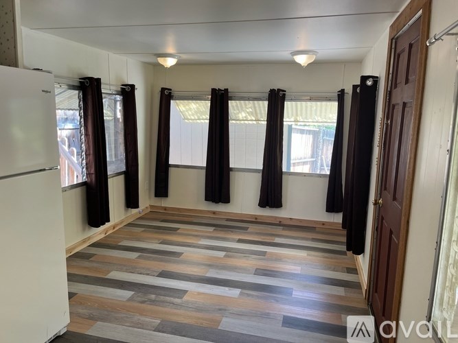 A room with wooden flooring and curtains on the windows.