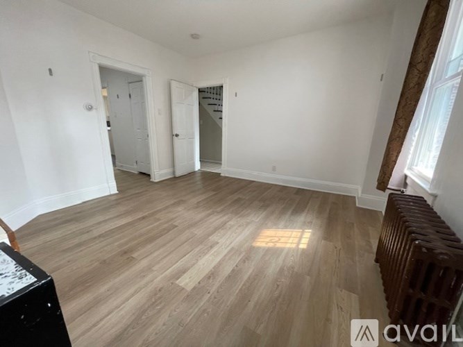 A room with wooden flooring and white walls, with a window on the right side.