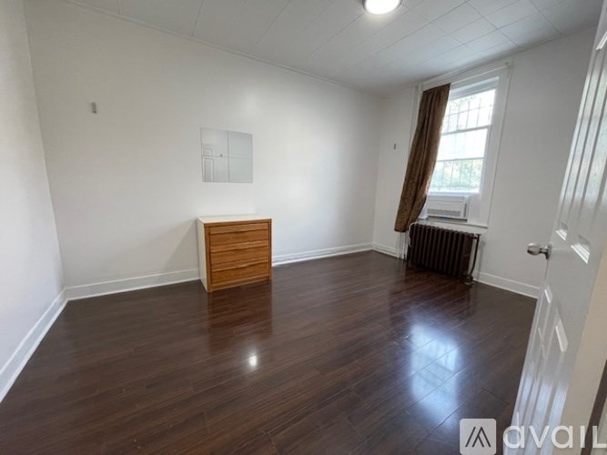A room with wooden flooring and a white wall with a brown curtain.