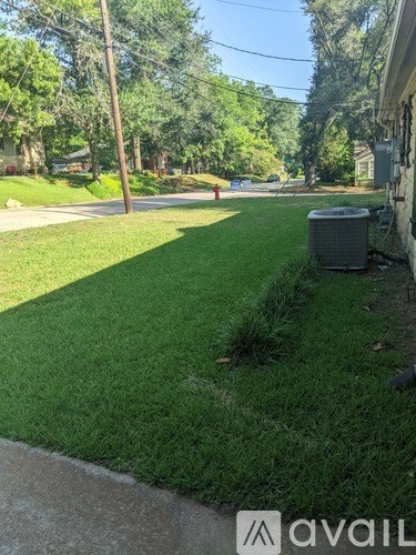 A residential street with a green lawn and a trash can.