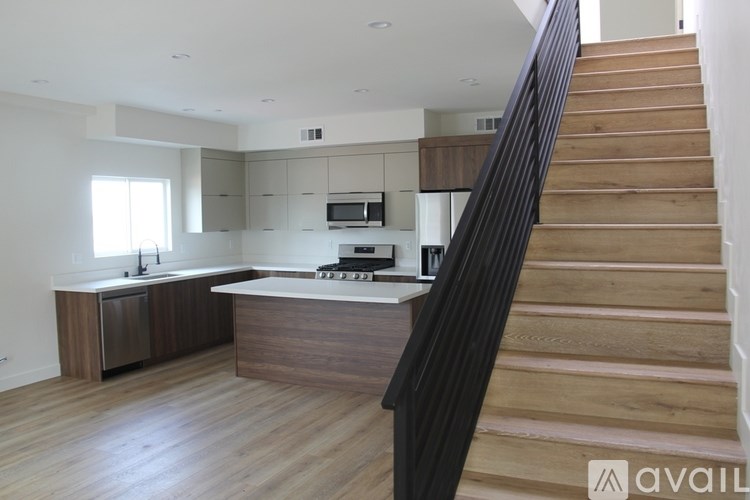 A modern kitchen with wooden floors and stairs leading to the upper level.