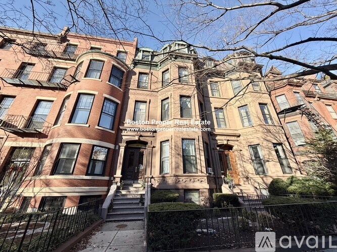 A row of brown and beige townhouses with black metal fences in front.