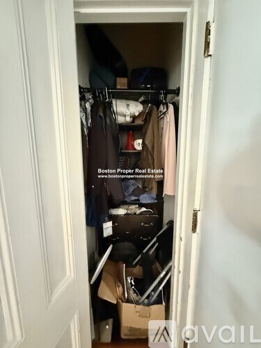 A small closet with clothes and a sign that says Boston Proper Real Estate.