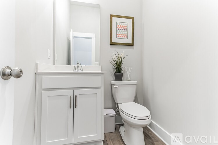 A white bathroom with a toilet, cabinet, and a plant.