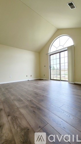 A room with wooden flooring and a large arched window.