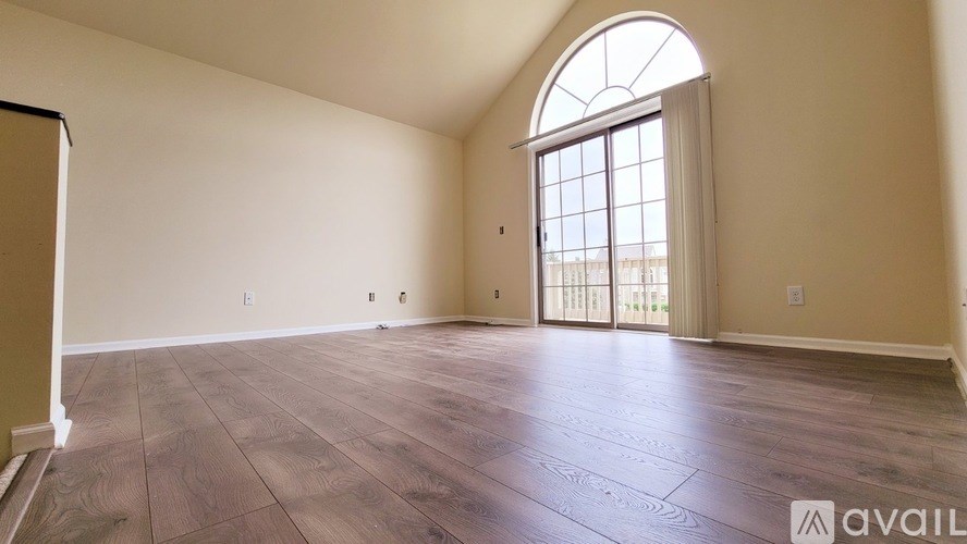 A spacious room with wooden flooring and a large arched window.