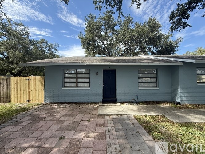 A house with a blue exterior and a black door is surrounded by a brick driveway.