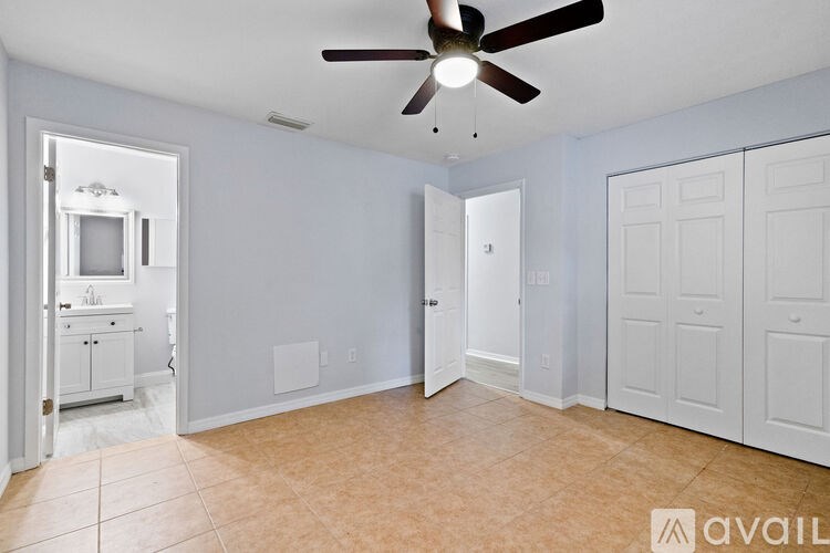 A room with a ceiling fan and a kitchen area in the background.