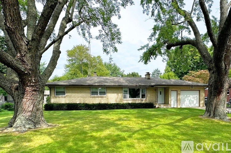 A house with a brown roof and a white garage door is surrounded by trees.