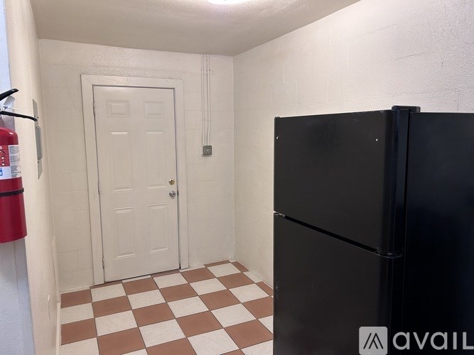 A black refrigerator sits in a room with a checkered floor and a white door.