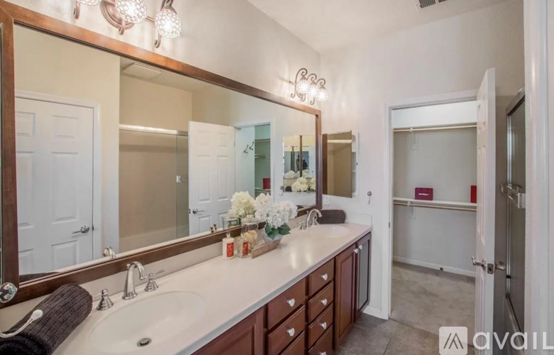 A bathroom with a large mirror, sink, and a vase of flowers.