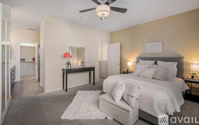 A bedroom with a large bed, a table with a vase of flowers, and a ceiling fan.