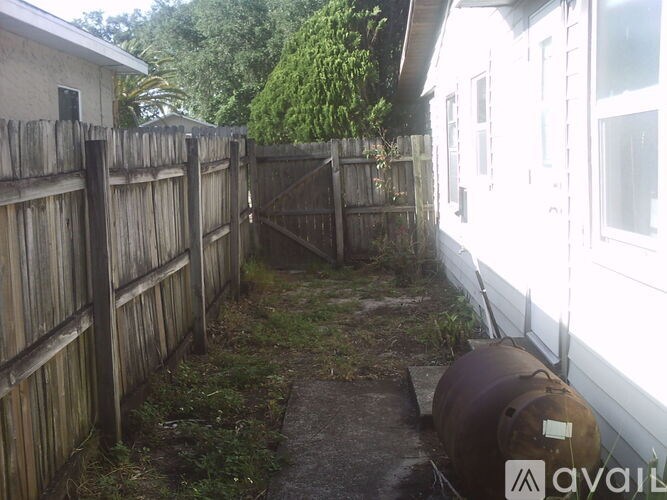 A rusty barrel sits in a backyard between two wooden fences.