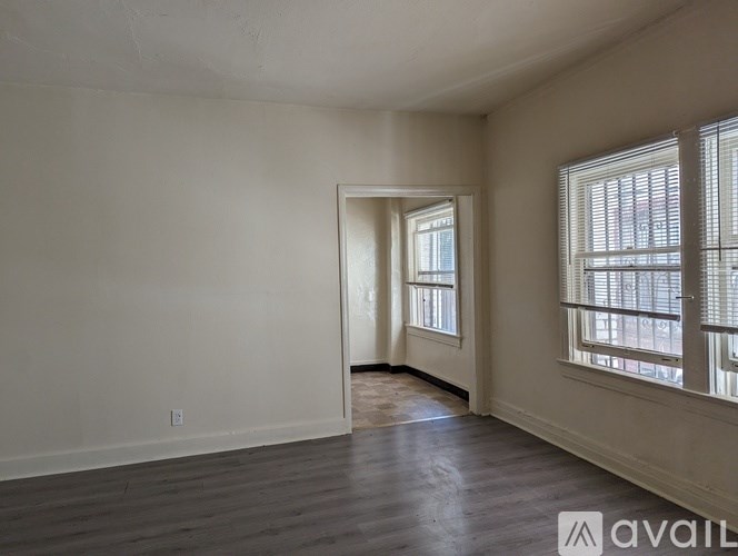 A room with a doorway leading to another room, wooden floors, and a window with blinds.