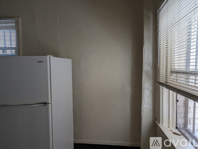 A white refrigerator sits in a room with a window covered in blinds.