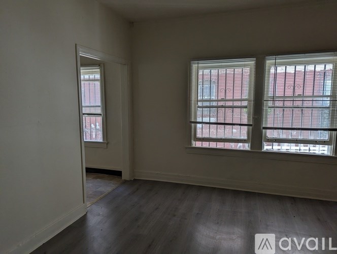 A room with two windows and wooden floors is available for rent.