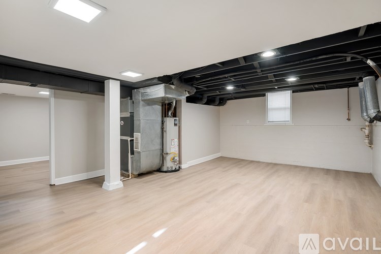 A spacious room with wooden flooring and white walls, featuring a large open doorway and a window.