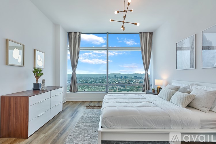 A bedroom with a large bed, a wooden dresser, and a view of the city from a large window.