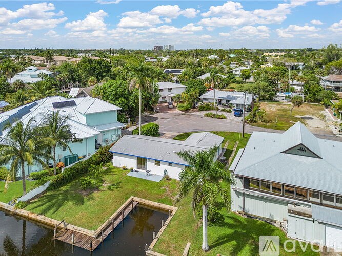 A house with a dock in front of it is surrounded by other houses and palm trees.