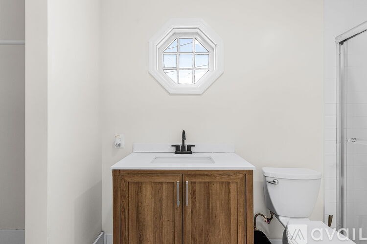 A bathroom with a hexagonal window above a sink and wooden cabinet.