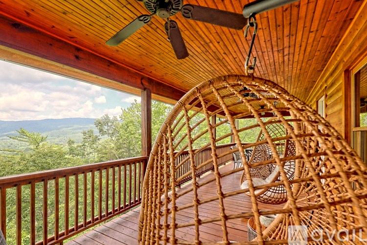 A wooden balcony with a fan and chairs overlooking a mountainous landscape.