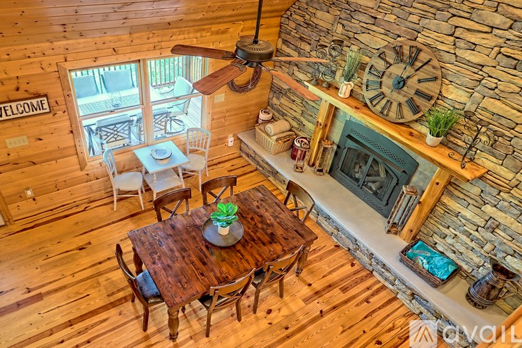 A wooden table with chairs and a fan in a room with a stone fireplace.