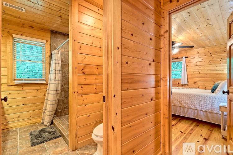 A wooden bathroom with a toilet, a window, and a bedroom.
