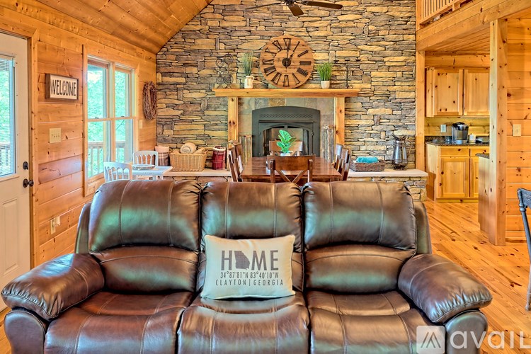 A leather sofa with a cushion that says "HOME" is in the foreground of a room with a stone fireplace and wooden floors.