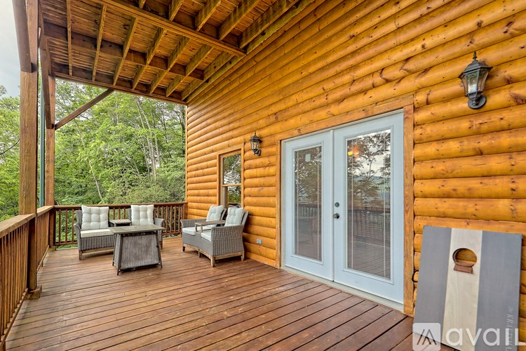A wooden deck with a couch, chairs, and a table is on the porch of a cabin.