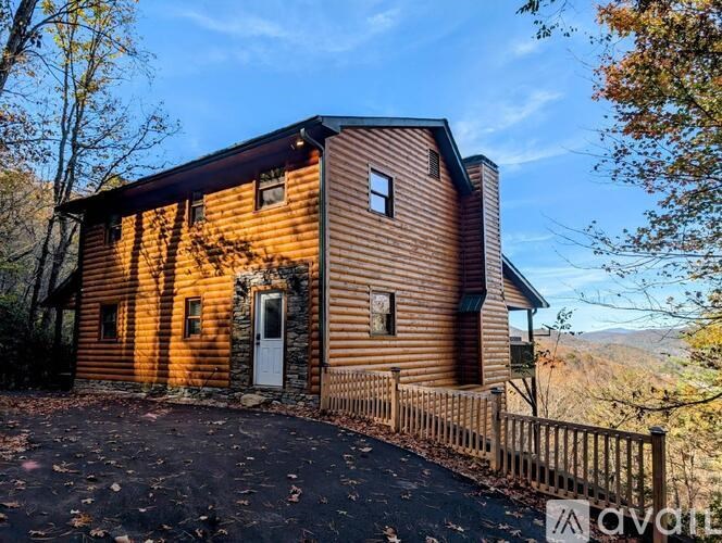 A wooden cabin with a white door and windows is surrounded by a wooden fence.