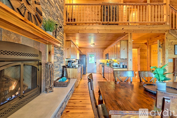 A large wooden dining table is surrounded by chairs in a spacious room with a stone fireplace.