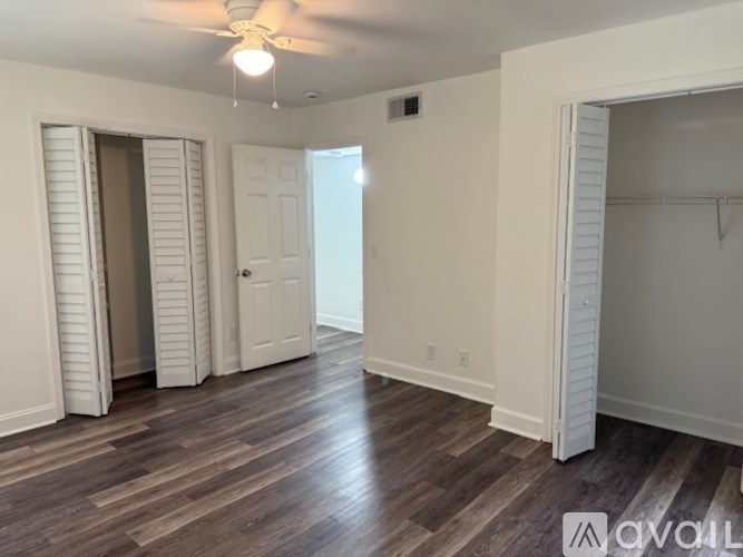 A room with white walls and wooden flooring, featuring a ceiling fan and a door.