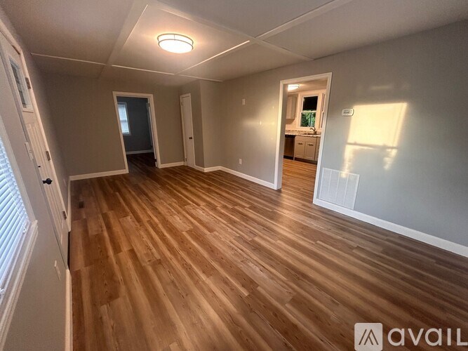 A room with wooden flooring and white walls, with a doorway leading to another room.