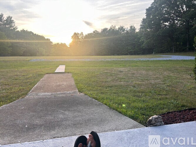 A concrete walkway leads through a grassy field with a sunset in the background.