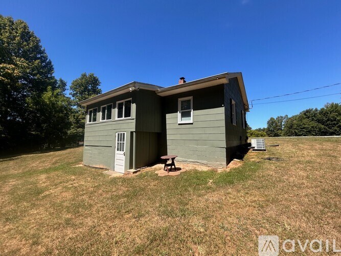 A small house with a porch and a picnic table sits in a grassy field.
