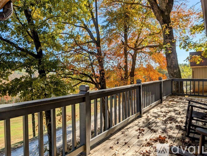 A wooden deck with a railing and a chair with fallen leaves on it.