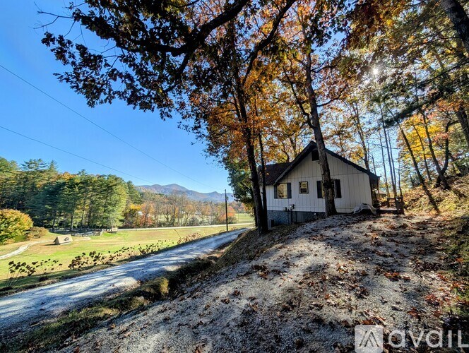 A small white house is nestled among trees with autumn leaves.