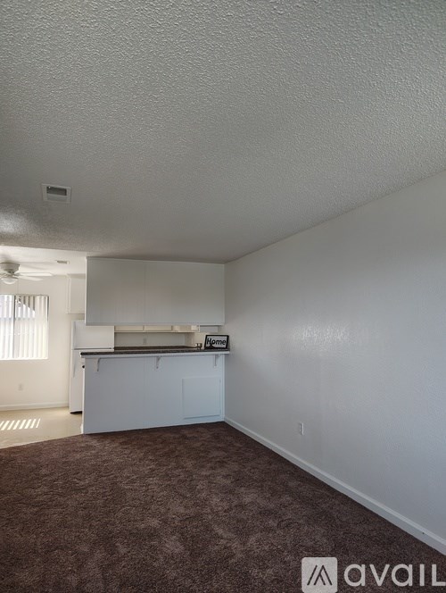 A room with a carpeted floor and a kitchenette.