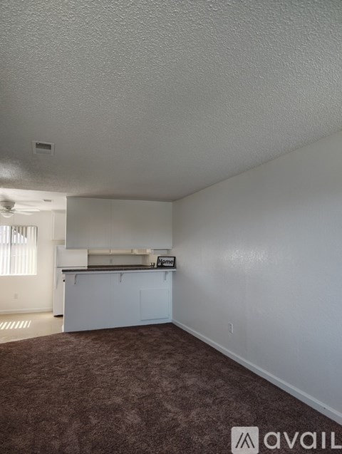 A room with a carpeted floor and a kitchenette.