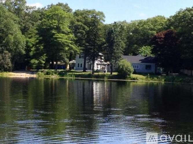 A serene lake surrounded by lush green trees and a white house in the distance.