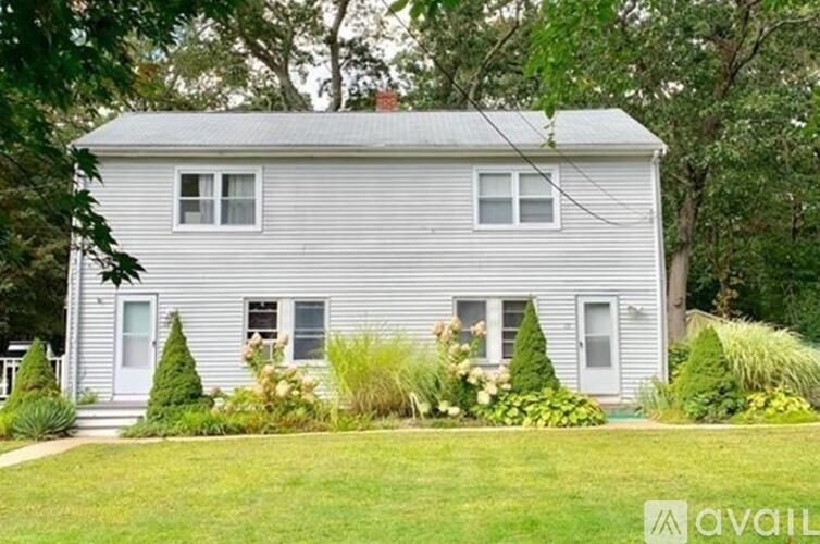 A house with a grey siding and a white door is surrounded by greenery.