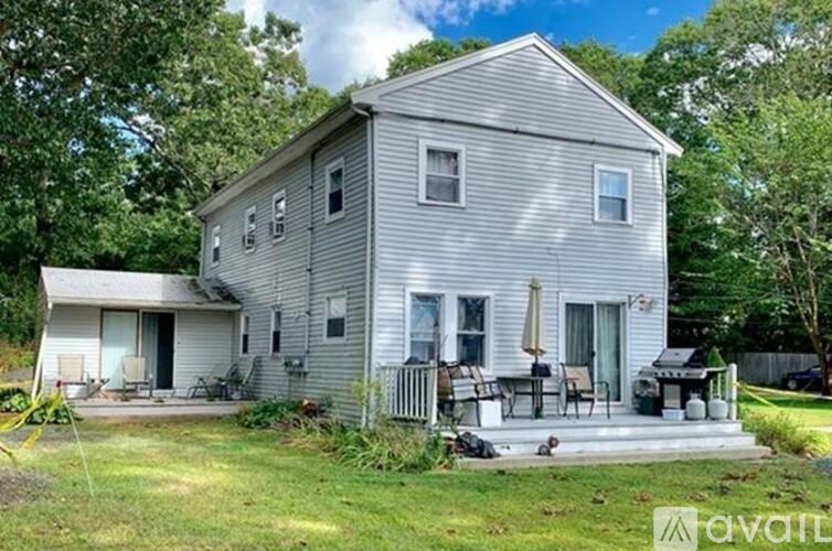 A house with a grey siding and a white door is surrounded by greenery.