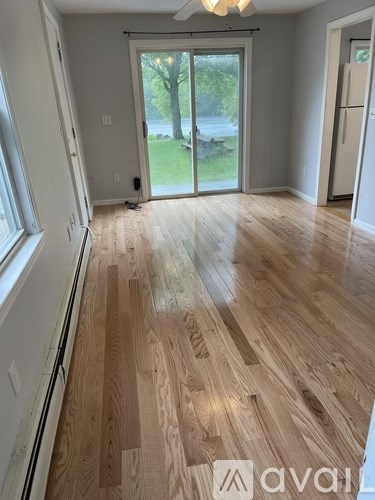 A room with wooden flooring and a sliding glass door leading to a backyard.