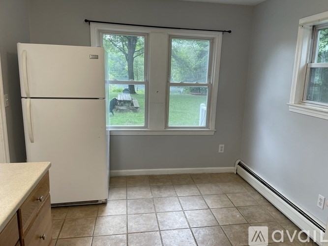 A kitchen with a white fridge and a window with a view of a lawn and trees.
