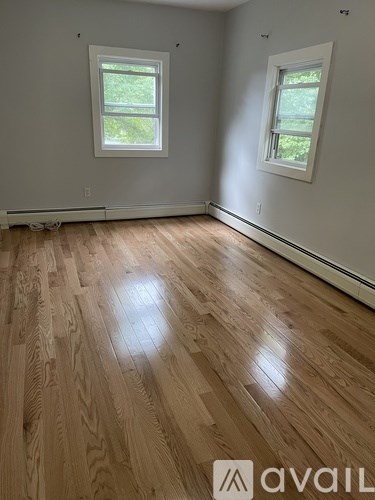 A room with wooden flooring and two windows.