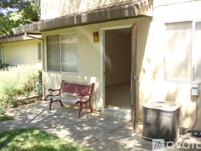 A red bench sits on a concrete patio in front of a tan house.