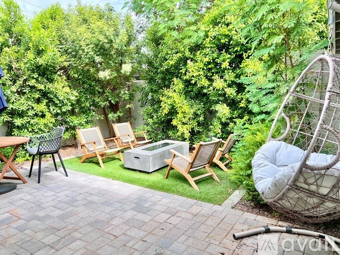 A patio with chairs and a table surrounded by greenery.