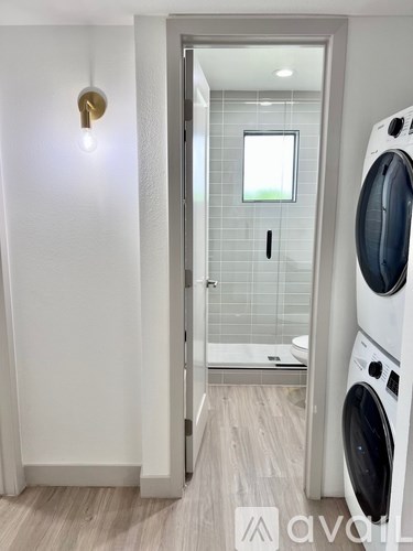 A white washing machine sits in a laundry room with a door open to a bathroom.