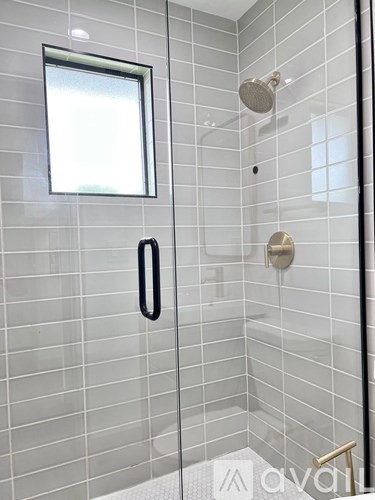 A modern bathroom with a glass shower door and a window.