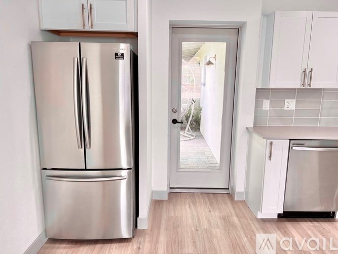 A modern kitchen with a stainless steel refrigerator and a white door.